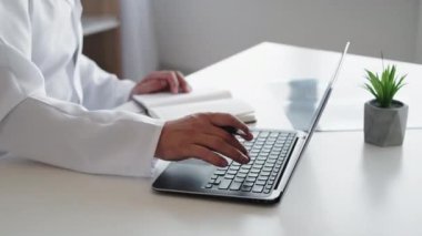 Çevrimiçi tanı. Elektronik tıbbi veriler. Dijital kayıt. Beyaz önlüklü tanınmayan erkek doktor modern işyerinde dizüstü bilgisayar kullanıyor..