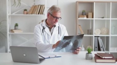 Teşhis radyolojisi. Göğüs muayenesi. Akciğer enfeksiyonu. Orta yaşlı erkek doktor akciğer röntgeni taraması yapıyor. Hafif modern işyerinde laptop kullanıyor..