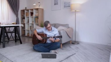 İnternetten ders. Erkek müzisyen. Evde eğitim. Akustik gitarla oynayan akıllı, konsantre olmuş orta yaşlı bir adam..