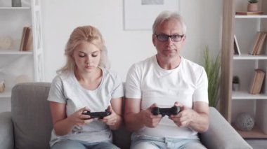 Ev yapımı video oyunu. Aile eğlencesi. Sanal ev eğlencesi. Şaşkın kız çocuğu orta yaşlı baba acemi oyuncular modern iç mekanda koltukta oyun pedlerini değiştirmeyi öğreniyor..