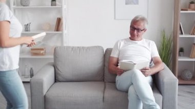 Okuma hobisi. Aile bağı. Akıllıca bir eğlence. Mutlu orta yaşlı baba kızı modern oturma odasındaki kanepede açık kitapla öğrenmenin keyfini çıkarıyor..