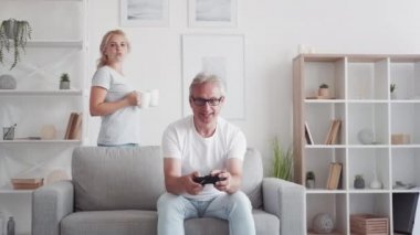 Aile çay molası. Hafta sonu tatili. Bakıcı kız, orta yaşlı babaya sıcak içecek servisi yapıyor. Modern oturma odasındaki koltukta video oyunu oynuyor..