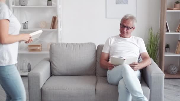阅读爱好 家庭联系 聪明的休闲 快乐聪明的中年父亲女儿喜欢在现代客厅的沙发上一起看书学习 — 图库视频影像
