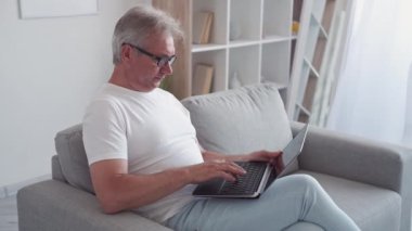 Yazılım sorunu. İnternetten iş stresi. Program hatası. Sistem virüsü. Sinirli, sinirli, orta yaşlı bir adam. Kırık dizüstü bilgisayarını açık evdeki koltukta kullanmaktan vazgeçti..