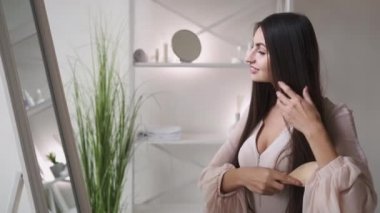 Kadın güzelliği. Sabah bakımı. Sağlıklı tedavi. Hoş, zarif bir kadın. Aynadan önce uzun, esmer saçlarını tarıyor..