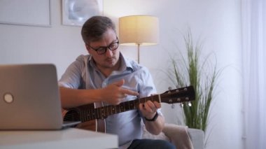 Gitar dersi. Erkek öğretmen. İnternetteki konferans. Masa lambasının iç tarafında akustik enstrüman çalmayı açıklayan orta yaşlı bir adamdan esinlendim..