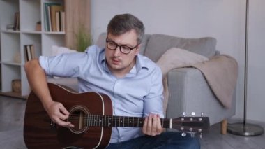 Müzikal hobi. İlham verici bir adam. Evde eğitim. Zeki, orta yaşlı bir adam, ışık odasının içinde oturup akustik gitar çalıyor..