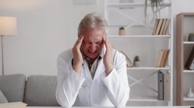 Doktor baş ağrısı. Tıbbi stres. Migren basıncı. Orta yaşlı hasta bir erkek pratisyen. Modern iş yerindeki tapınaklara masaj yapıyor..