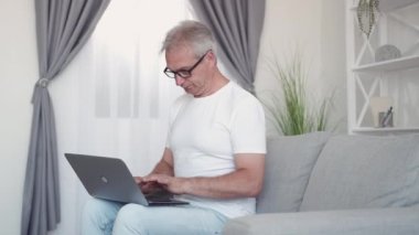 Sanal tartışma. İş çatışması. İnternet kaygısı. Huzursuz son sınıf öğrencisi modern iç mekandaki kanepede dizüstü bilgisayar kullanarak mesaj okuyor..