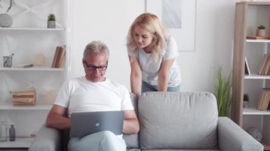Aile desteği. Başarılı çevrimiçi proje. Uzaktan çalışma. Kızının keyfi yerine geliyor. Orta yaşlı baba, modern iç mekandaki koltukta dizüstü bilgisayar kullanıyor..