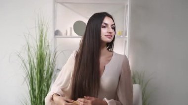 Saç stili tedavisi. Rahat kadın. İyi akşamlar güzellik servisi. Güzel, güler yüzlü bir bayan iç mekânda düz, uzun, esmer saçları tarıyor..