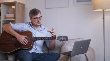 Müzik okulu. Erkek öğretmen. Online eğitim. Orta yaşlı bir adam dizüstü bilgisayarda akustik gitar çalma kurallarını anlatıyor..