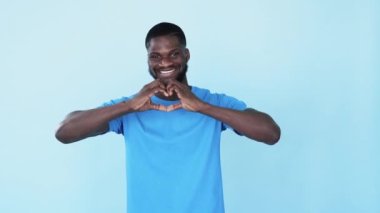 Destekleyici siyah adam. Kalp hareketi. Irksal hoşgörü. Blm bakımı. Minnettar, mutlu, gülümseyen Afrikalı adam mavi fotokopi arkaplanındaki aşk işaretini paylaşıyor..