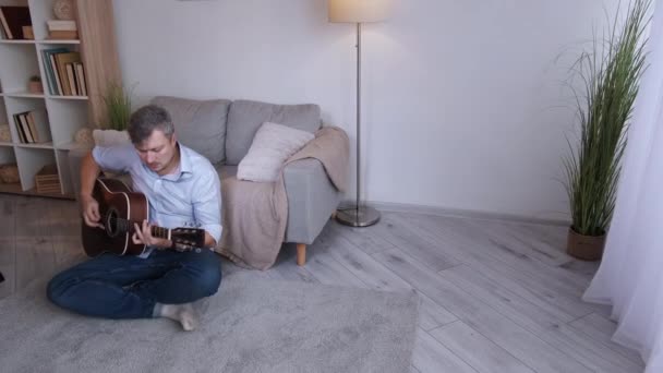 家庭休闲 男音乐家 缪斯的灵感 中年男人坐在地板上 在光线室室内的复制空间中弹奏声吉他 — 图库视频影像