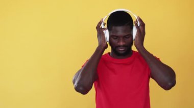 Müzik ilhamı. Kablosuz teknoloji. Pozitif enerji. Rahat siyah adam, kulaklık takıp dans etmekten zevk alıyor. Parlak sarı arka planda izole edilmiş bir melodi..