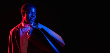 Kara Cuma. Alış veriş afişi. Siber Pazartesi. İndirimli reklam. Modaya uygun bir milenyum adamı, neon ışıklı siyah fotokopi arka planında alışveriş torbaları tutuyor..