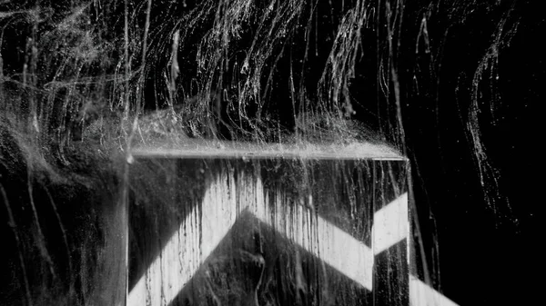 Water splash. Fluid drip motion. Grunge texture. White black ink drop splatter on glowing glass cube edge on dark abstract background.
