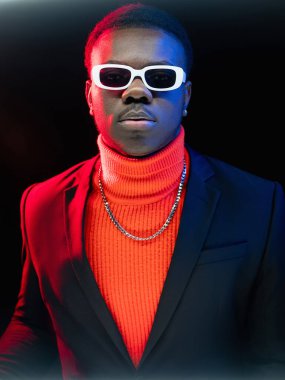 Gece modası. Başarılı bir adam. Neon ışığı insanları. Şık takım elbiseli yakışıklı, kendine güveni tam bir erkek portresi. Renkli kırmızı gözlüklü, koyu renk arka planda gözlüklü..