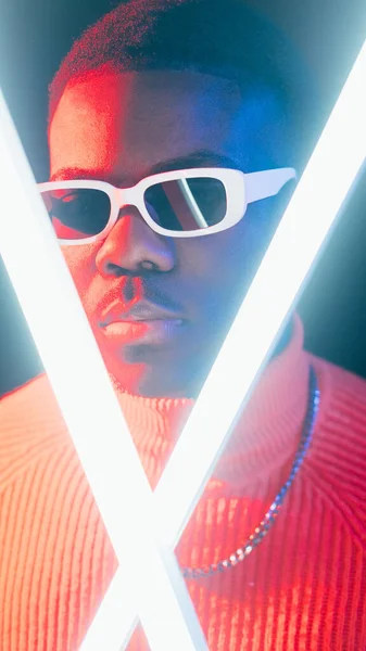 Futuristic portrait. Neon light man. Cyber punk. Confident serious stylish guy face in sunglasses bright LED glow on dark studio background.