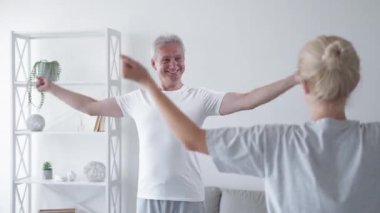 Kişisel antrenman. Ev sporu. Beden eğitimi dersi. Ateşli orta yaşlı bir adam hafif iç mekanda kadın eğitmenle kol eklem egzersizi yapıyor..