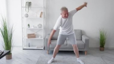 Sabah sporu. Ev pilatesi. Yoga eğitimi. Gülümseyen orta yaşlı, esinlenmiş, orta yaşlı, kıvrımlar yapan, sırt kaslarını esneten, hafif oturma odasında egzersiz yapan bir adamdan esinlendim..