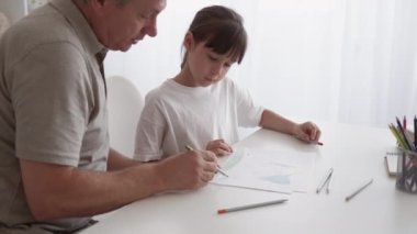 Sanat eğitimi. Çocuk çizimi. Yaratıcı çocuk hobisi. Aile eğlencesi. Orta yaşlı bir baba, yetenekli küçük bir kızın evde renkli kalemler çizmesine yardım ediyor..