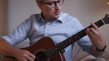 Gitar dersi. Gergin adam. Evde eğitim. Yakışıklı, orta yaşlı, gündelik bir adam. Koltukta oturmuş, ışık odasının içinde müzik aleti çalıyor..