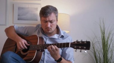 Müzikal hobi. İlham verici bir adam. Hayatın tadını çıkarıyorum. Yakışıklı, orta yaşlı, rahat, rahat, koltukta oturup gitar çalan, aydınlık odada eğlenen bir adam..