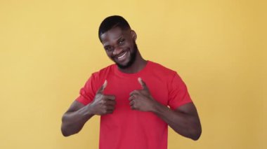 Jest gibi. Irksal hoşgörü. Siyahların hayatı önemlidir. Cesaretlendirmeyi destekle. Dost canlısı, neşeli, Afrikalı bir adam, turuncu boş bir arka planda baş parmağıyla kabul ediyor..