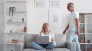 Çevrimiçi gizlilik. Gizli içerik. Aile müdahalesi. Orta yaşlı babadan bilgisayar ekranı saklayan sorunlu bir kız modern iç mekanda yürüyor..