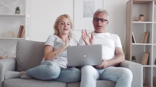 家族のビデオ通話 ホーム仮想チャット 通信距離 リラックスした幸せな中年のお父さん娘手を振ってこんにちはスピーキング上のラップトップカメラオンソファで現代的なインテリア — ストック動画