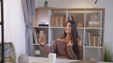 Çevrimiçi iletişim. Güzel kadın. Mobil bağlantı. Mutlu kahkahalarla gülen kadın evde oturmuş, aydınlık odada akıllı telefonlardan konuşuyor..