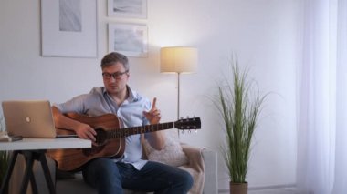 Müzik dersi. Erkek öğretmen. Çevrimiçi toplantı. Orta yaşlı bir adam dizüstü bilgisayarda akustik gitar çalma kurallarını anlatıyor..