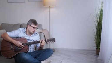 Müzik ilhamı. Erkek oyuncu. Evde öğrenim. Zeki, orta yaşlı bir adam, oturma odasında akustik gitar çalmaya katılıyor..