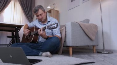 İnternetten ders. Çaresiz adam. Eğitimsel bir sorun. Keyifsiz orta yaşlı bir adam oturmuş bilgisayar başında öğreniyor ve iç mekânda gitar çalıyor..