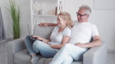 Eğlenceli aile hafta sonu. Çevrimiçi ev eğlencesi. İnternet eğlencesi. Rahatlamış orta yaşlı baba kızı modern iç mekandaki kanepede dizüstü bilgisayar kullanarak komedi programı izlemekten zevk alıyor..