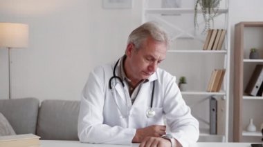 Sıkılmış doktor. Gün bitiminde. TeleHealth toplantısı. Sinirli orta yaşlı doktor hasta şikayetinden yorulmuş çalışma yerinden ayrılan saate bakıyor..