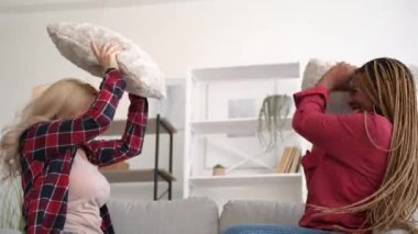 Kızlar yastık savaşı. Eğlenceli bir ev eğlencesi. Pijama partisi. İki heyecanlı, neşeli, çeşitli bayan arkadaş oturma odasındaki kanepede gülüp eğleniyorlar..