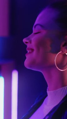 Neon ışıklı parti. Dans eden kadın. Hayatın tadını çıkarıyorum. Mutlu güzel bayan mor parıltılı aynaya bakarak müziğe devam ediyor. Dikey video.