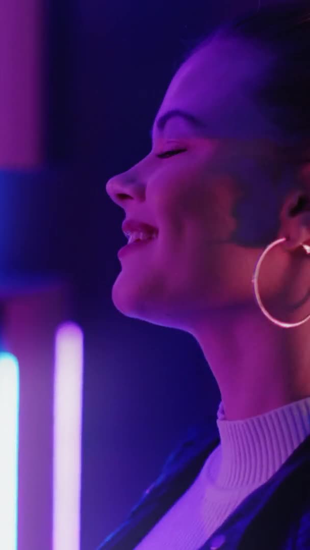 ネオンパーティーだ 踊る女性 人生を楽しんで 紫の光の中で鏡を見て音楽に感動する幸せな女性 垂直ビデオ — ストック動画