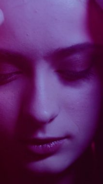 Kadın büyüsü. Şehvetli güzellik. Neon ışıklı portre. Pembe parıltılı zarif bir kadın uzun saçlarıyla ilgileniyor. Dikey video.