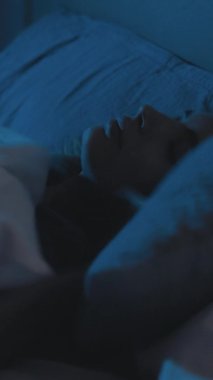 Uyku sorunu. Rahatsız bir kadın. Uyku vakti. Yorgun, gözleri kapalı, karanlık bir evde yatakta yatan bir kadın. Dikey video.