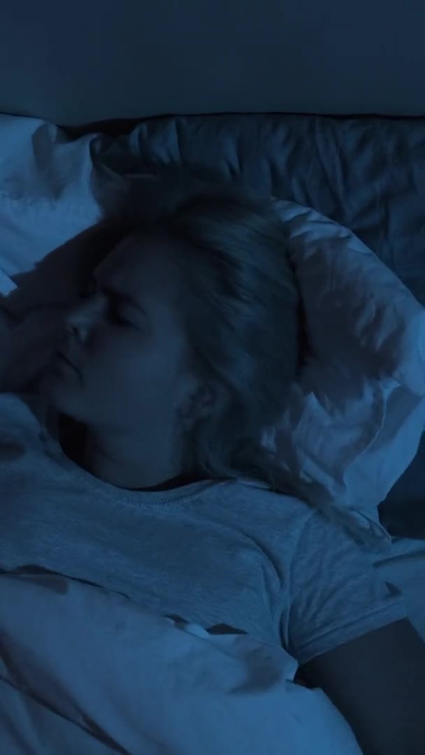 夜の恐怖 悪い夢だ 悪夢のような不安 暗い青色の光の中で夜遅くにベッドの中で一人で寝て回る投げ乱れた女性 垂直ビデオ — ストック動画