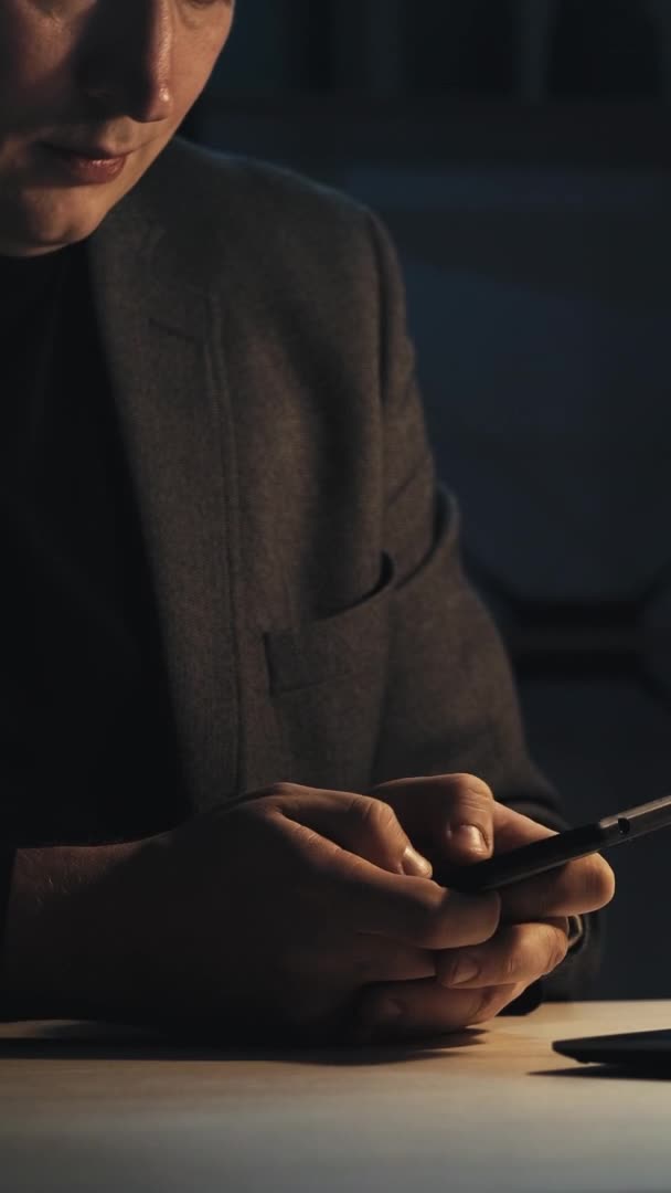 夜のビジネスチャット 携帯電話の仕事 遅いオンラインコミュニケーション 暗い職場で電話のメッセージを使用して執行人 垂直ビデオ — ストック動画