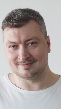 Pozitif adam. İyi sabahlar. Keyifli bir an. Beyaz tişörtlü, arka planda gülümseyen yakışıklı adam. Dikey video.