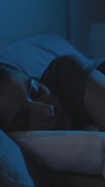 Uyku sorunu. Rahatsız bir kadın. Uyku vakti. Yorgun, gözleri kapalı, karanlık bir evde yatakta yatan bir kadın. Dikey video.