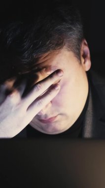 Aşırı çalışma yorgunluğu. Gece uykusuzluğu. Dijital göz yorgunluğu. Yorgun, uykulu iş adamı geç saatlere kadar bilgisayarla çalışıp karanlık işyerinde esnemekten yoruldu. Dikey video.