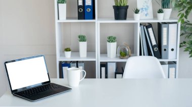 Office work. Computer mockup. Online technology. Opened laptop with blank screen staying on desk with cup of coffee in light room interior.