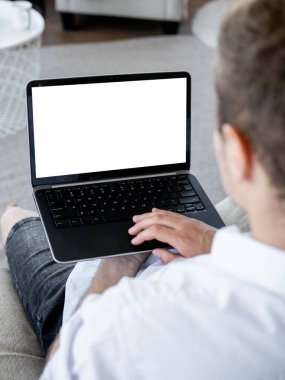 Distance work. Casual man. Computer mockup. Unrecognizable relaxed guy searching laptop with blank screen sitting light office room interior.