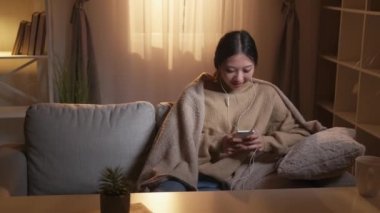 Müzik uygulaması. Hafta sonu çalma listesi. Samimi bir ortam. Gadget insanları. Rahatlamış mutlu kız Hygge Home iç mekanında cep telefonu kullanarak kulaklıklarda mp3 sesi dinlemekten zevk alıyor..